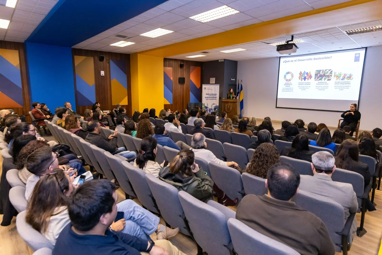 Vista del auditorio con el público asistente y la presentación proyectada al fondo.