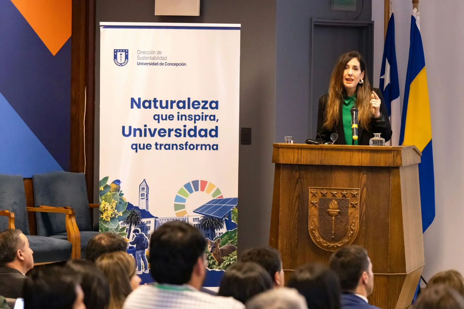 Paloma Toranzos en el podio del auditorio, junto al pendón «Naturaleza que inspira, Universidad que transforma».