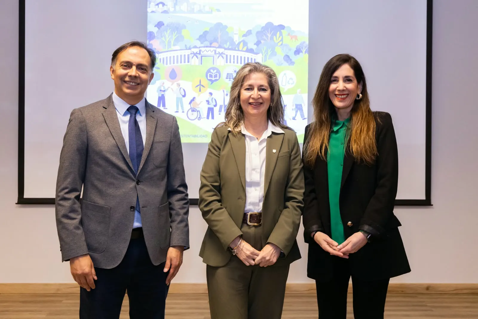 Tres personas posan sonrientes frente a la pantalla con la ilustración del Mes de la Sustentabilidad; Paloma Toranzos está a la derecha.
