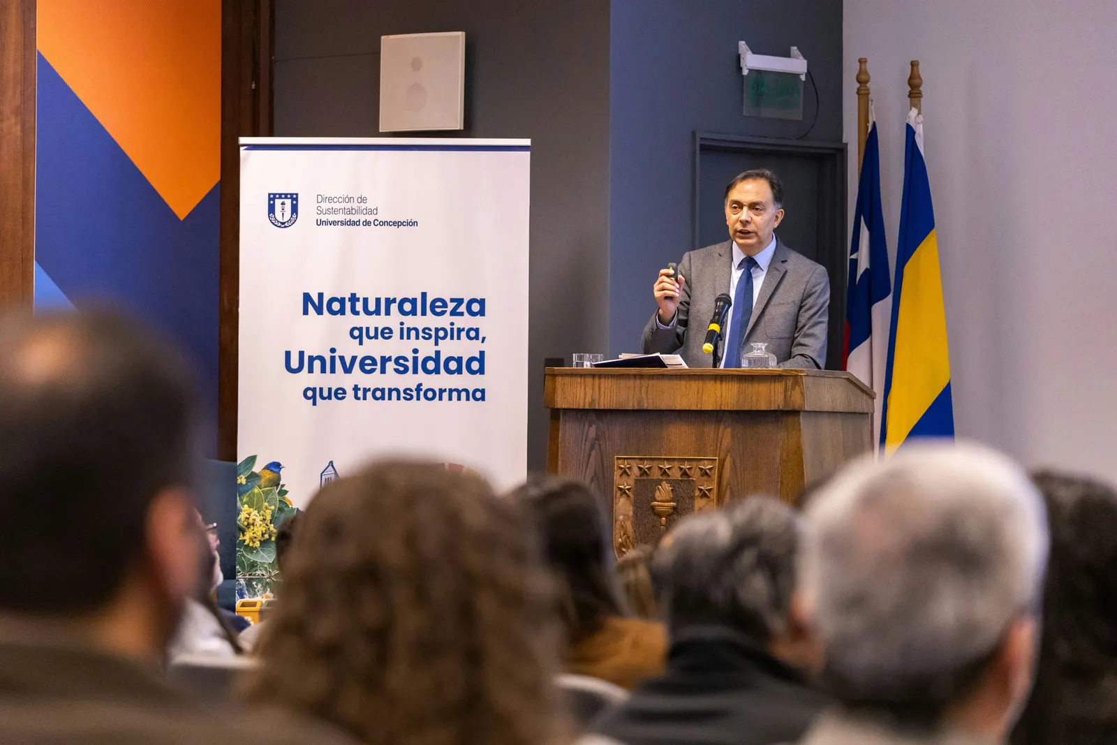Un expositor habla desde el podio, junto al pendón de la campaña y las banderas.