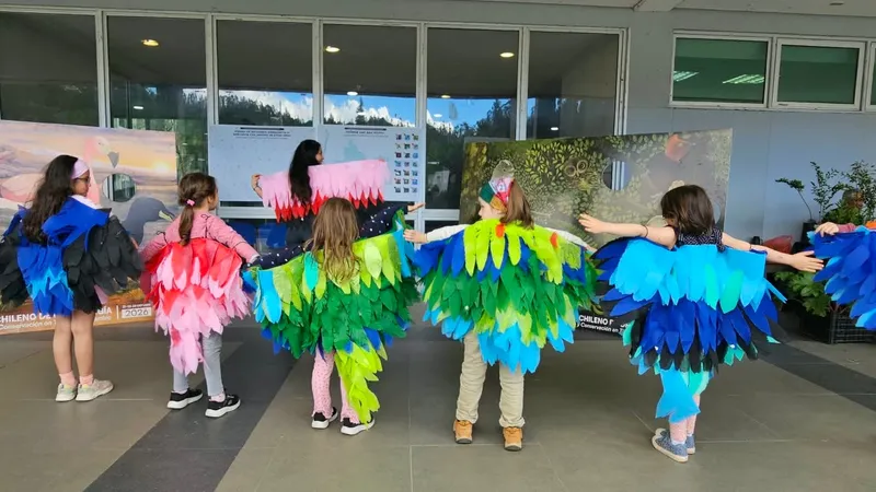 Un grupo de niñas y niños de espaldas, con alas de papel de colores y los brazos abiertos, en la Plaza de Pichones.